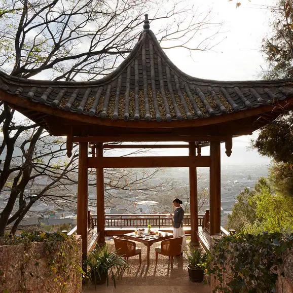 Wooden pavilion with upturned eaves at Amandayan, overlooking misty valley landscape.