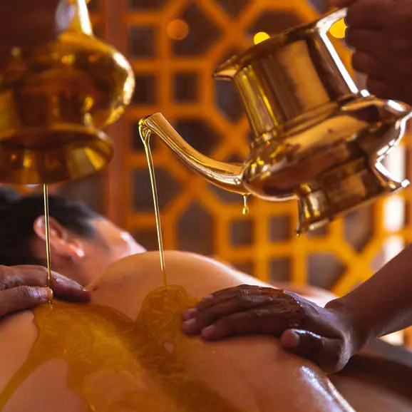 Warm oil being poured onto hands during a wellness treatment at Amanbagh.