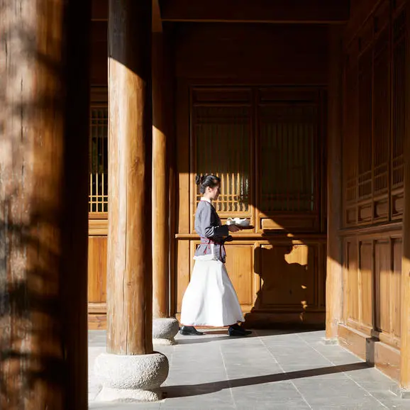 Staff member in traditional white dress standing in sunlit wooden corridor at Amandayan.