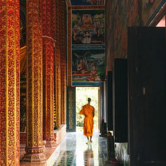 Buddhist monk in saffron robes walking through a golden-lit hallway at Amansara, Cambodia.