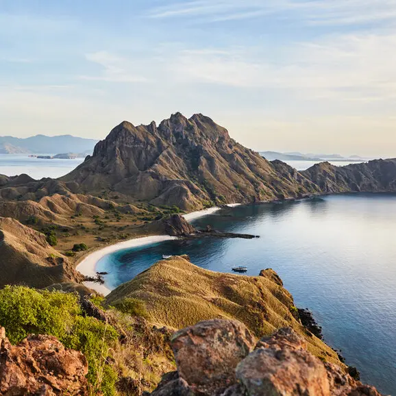 Aerial view of Amandira's rugged coastline with golden cliffs overlooking a crescent bay and blue waters.