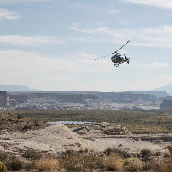 Helicopter flying over desert landscape near Amangiri, with distant mountains under cloudy sky.