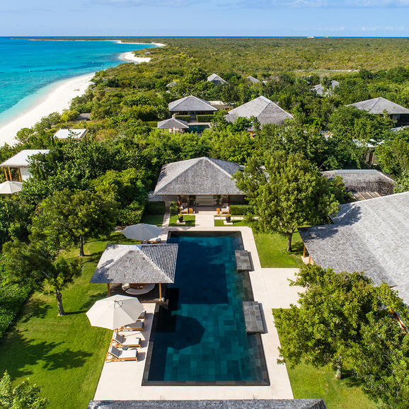 Aerial view of a six-bedroom villa at Amanyara surrounded by tropical vegetation, with a linear pool and beach beyond.