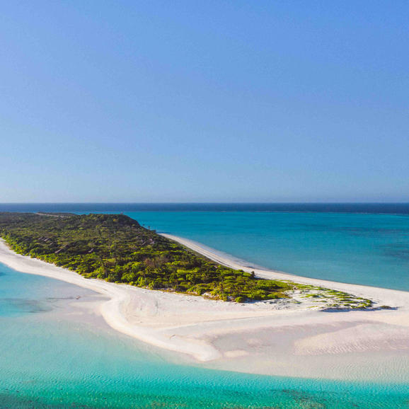 Aerial view of Pamalican Island at Amanpulo, showing white sand beach, turquoise waters and forested headland.
