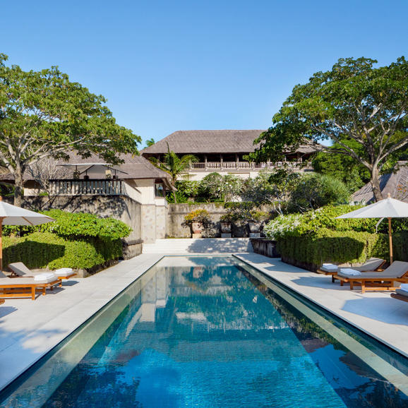 Lap pool flanked by tropical gardens at Aman Villas at Nusa Dua, with villa structures visible beyond.