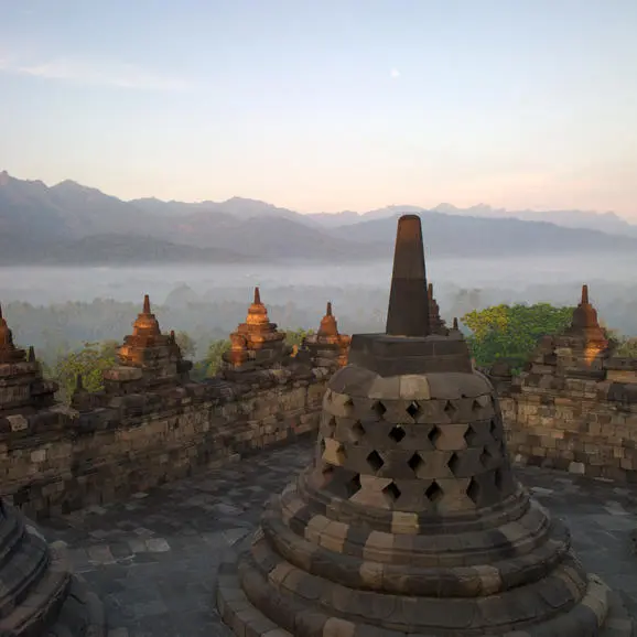 Borobudur Temple's stone stupas at sunrise, with misty volcanic landscape beyond, Indonesia.