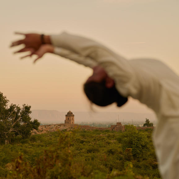 Yoga practitioner in white clothing performing a backbend at Amanbagh, with desert landscape visible beyond.