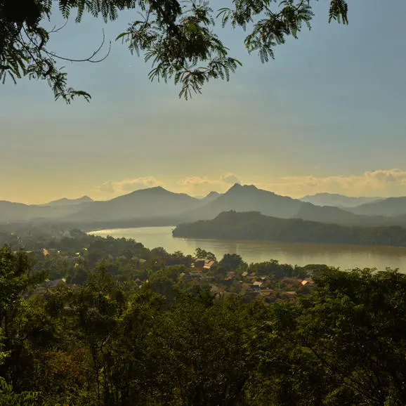 Aerial view of Phousi Temple viewpoint at Amantaka, Laos, with forested landscape and distant mountains at dawn.