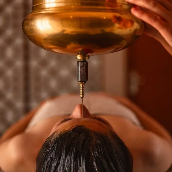 Shirodhara treatment at Amanbagh, with warm oil being poured onto a guest's forehead.