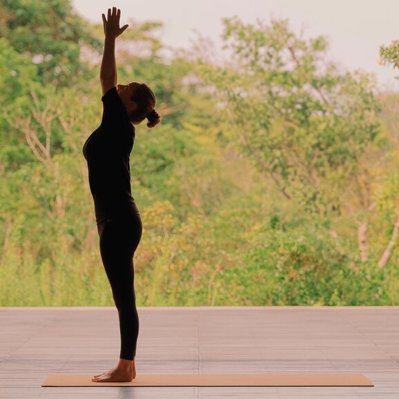 Silhouetted figure in yoga pose on wooden deck at Amanemu, Japan, with blurred natural landscape behind.