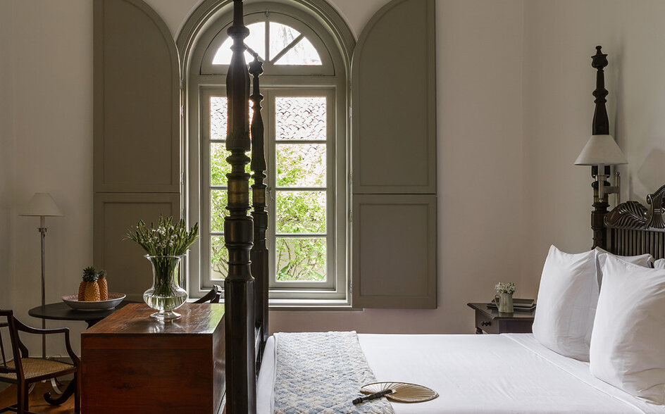 Principal bedroom at Amangalla with four-poster bed and arched window overlooking gardens.