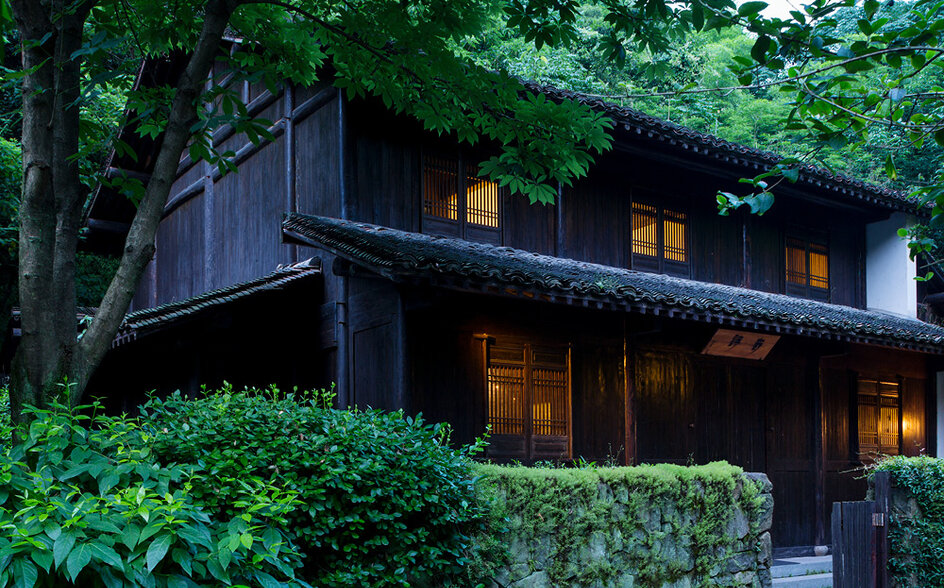 Traditional dark-timber villa surrounded by lush greenery at Amanfayun, evening light glowing from windows.