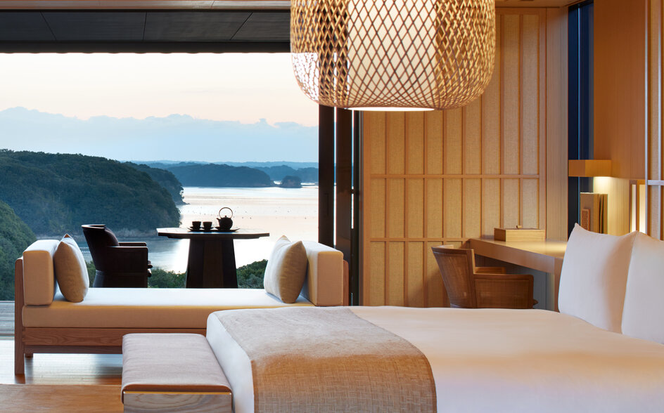 Nagi Suite bedroom at Amanemu overlooking the bay, with floor-to-ceiling windows and minimalist furnishings.