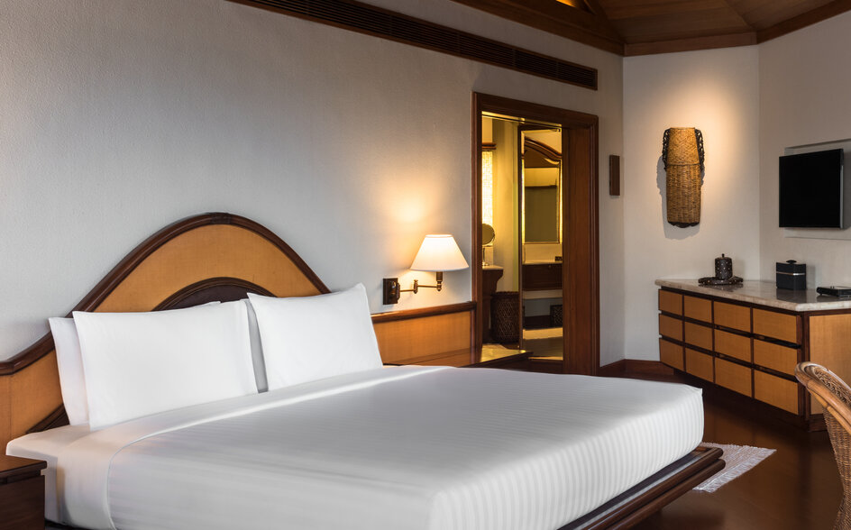 Hillside Casita bedroom at Amanpulo with wooden bed frame, white bedding, and warm lighting from wall sconces.