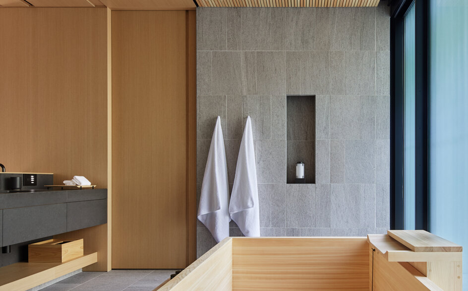 Wooden soaking tub beside floor-to-ceiling windows in a spa bathroom at Aman Kyoto, with natural materials and minimalist design.