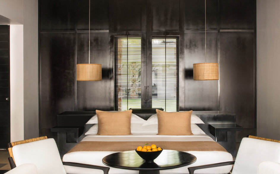 Bedroom at Amansara with black-framed glass partition, natural wood furniture, and contemporary pendant lighting.