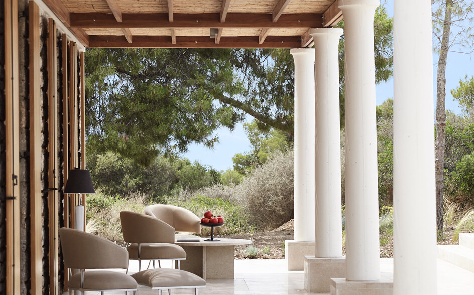 Columned terrace overlooking gardens at Amanzoe resort, with dining area and seating.