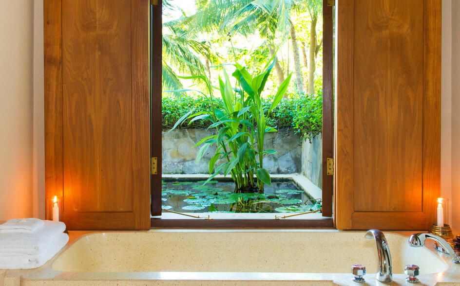 アマンキラ リゾートの浴室。木製の扉に囲まれた窓から緑の庭園が見え、バスタブの上に配置されている。