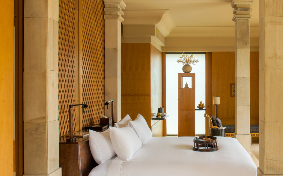 安缦齐和度假村的卧室，白色床铺位于柱廊中央，两侧为木制屏风和米色墙壁。