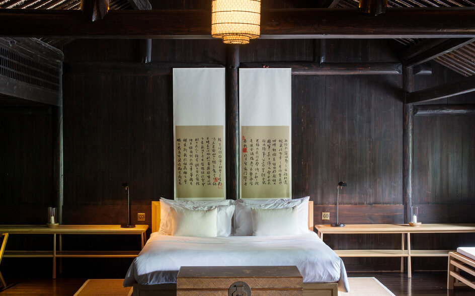 Principal bedroom at Amanfayun villa with wooden bed and dark timber ceiling beams.