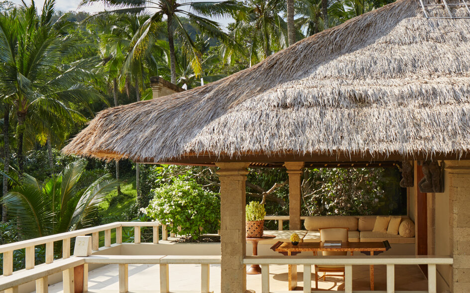 アマンキラ リゾートのガーデンスイートテラス。茅葺き屋根の建物、白い欄干、椰子の木が見える。