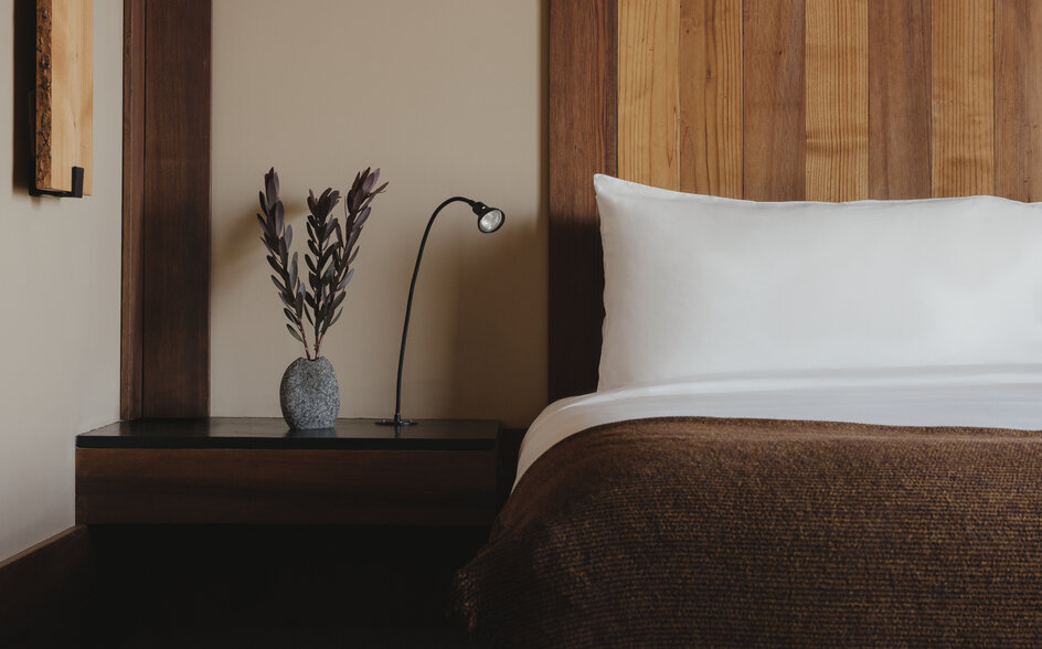 Bedside table with vase and reading lamp beside bed with white pillows at Amangani.