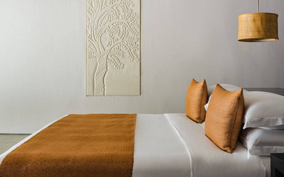 Principal bedroom at Amansara with ochre bedding, decorative cushions, and botanical wall art.