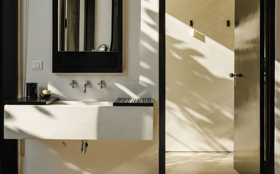Amansara bathroom with floating white sink, black-framed mirror, and glass-enclosed shower filled with natural light.