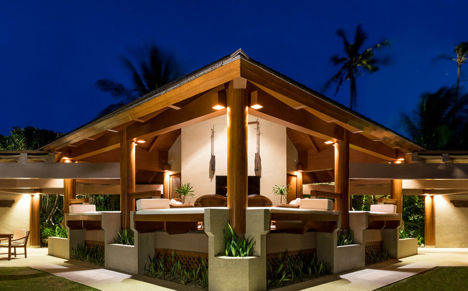 Amanpulo 리조트의 원침실 빌라 다이닝 파빌리온, 황금빛 조명이 켜진 목재 구조로 저녁 하늘을 배경으로.