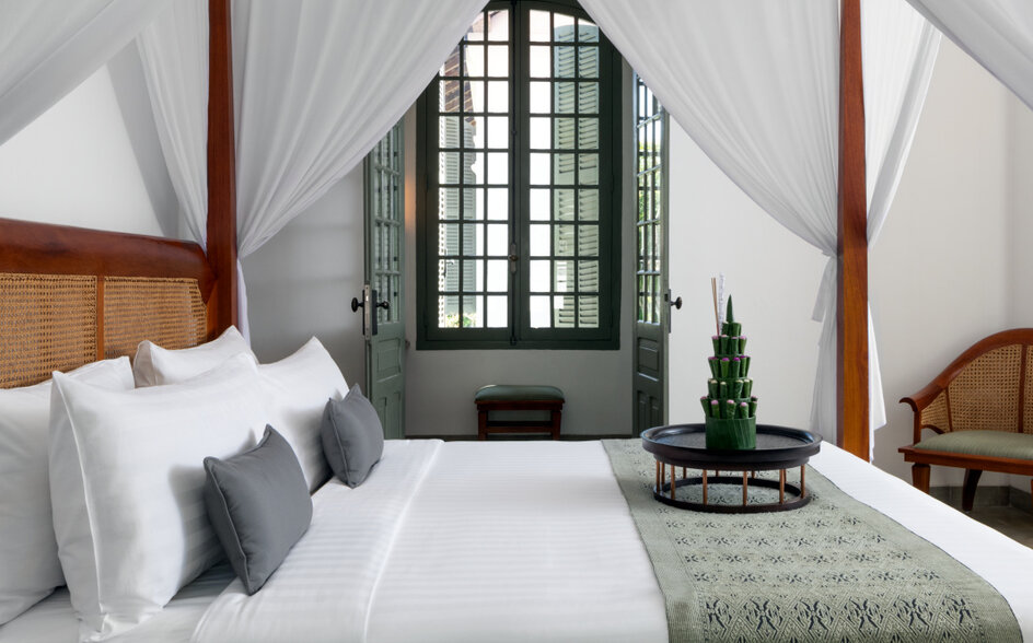 Principal bedroom with four-poster bed, white linens, and arched window at Amantaka.