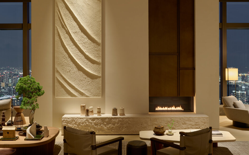 Communal lounge at Aman Tokyo with curved wall art, olive chairs, and city views.