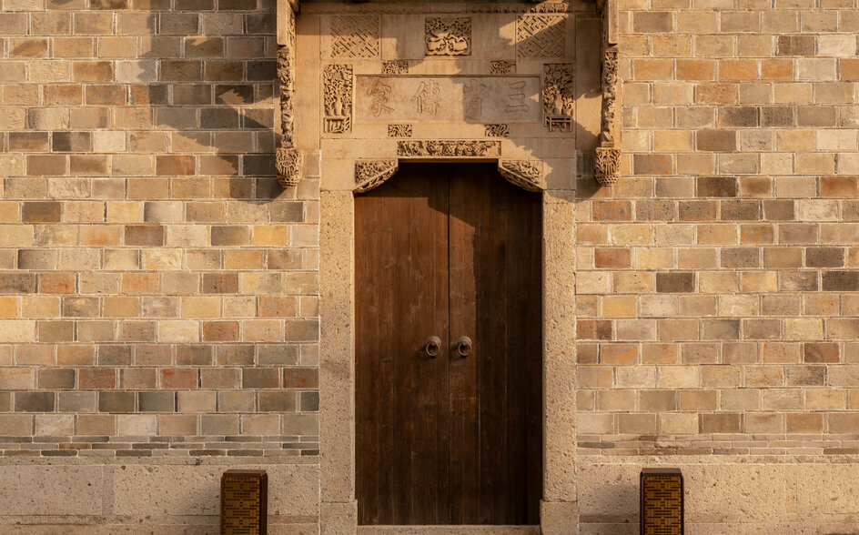Antique villa entrance door at Amanyangyun, with dark wooden door set in terracotta brick wall and stone bollards.