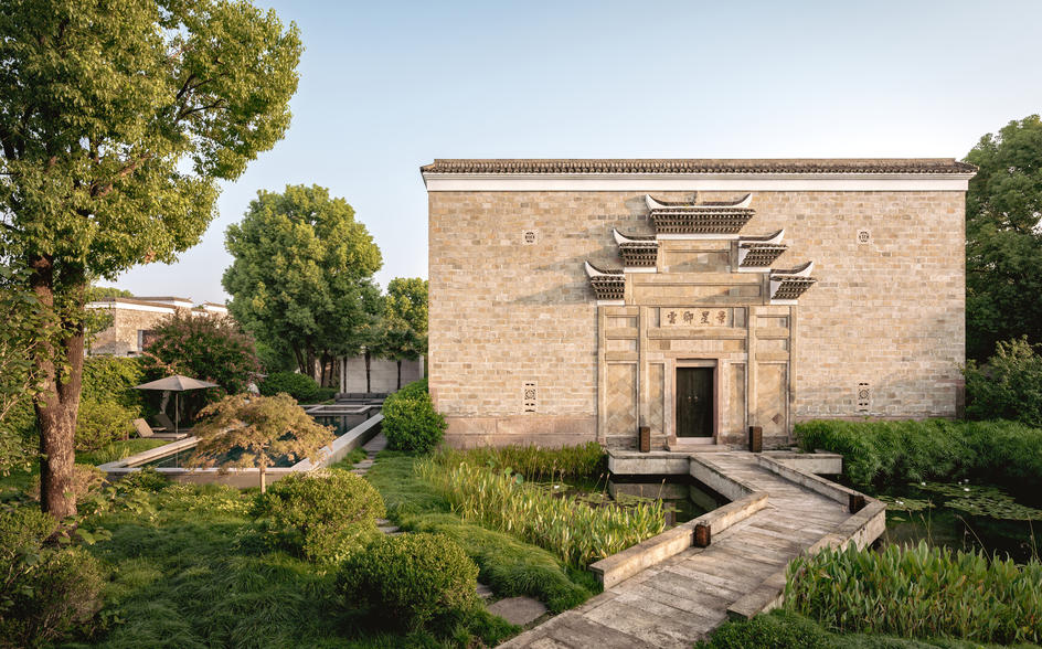 养云安缦度假村的砖砌建筑外观，周围绿树环绕，宽敞的石板路通向入口。