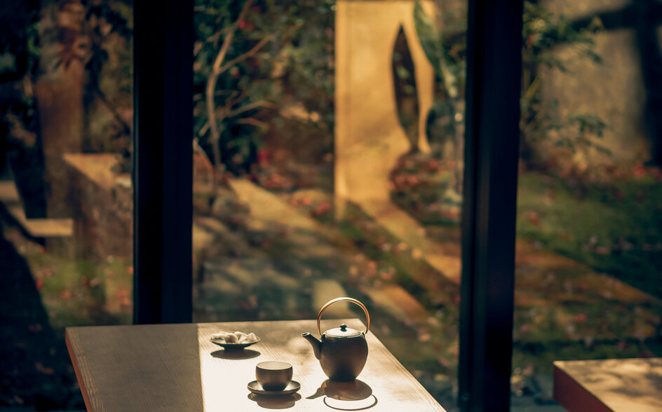 Afternoon tea service at a window table at Aman Kyoto resort, with sunlit garden views through glass panels.