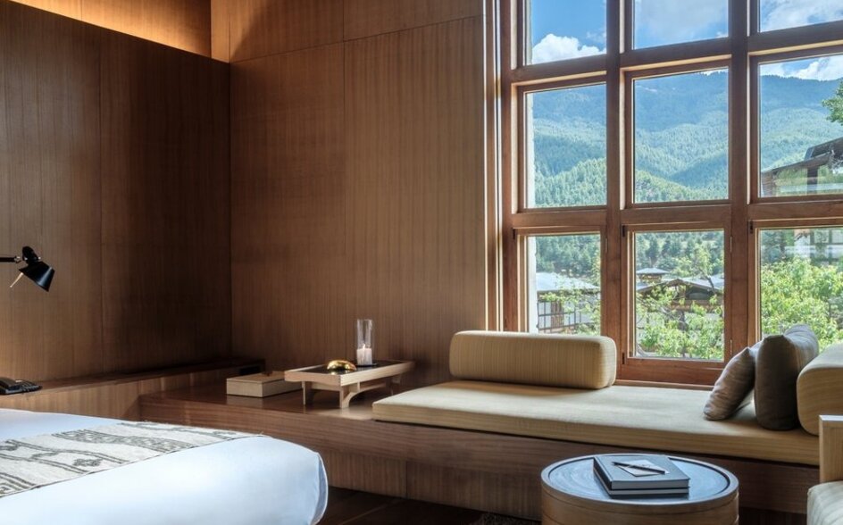 Amankora suite bedroom in Bumthang with low platform bed, wooden desk and large windows overlooking mountain landscape.