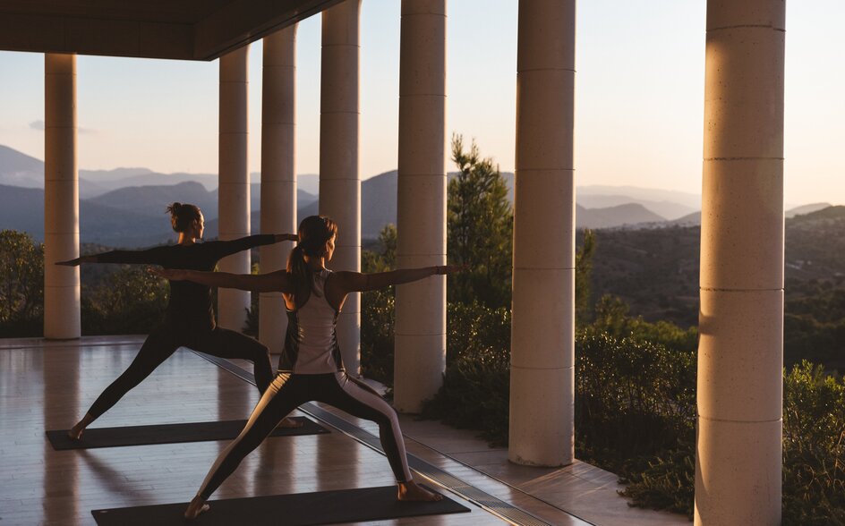 Sunrise yoga session at Amanzoe with floor-to-ceiling windows overlooking Greek hills.