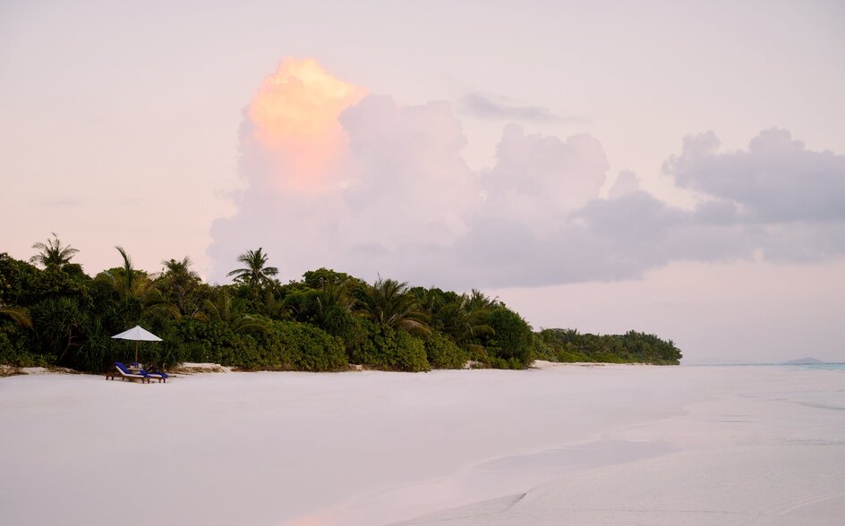 Amanpulo's island shoreline at dawn, with tropical vegetation and calm waters beneath a soft sky.