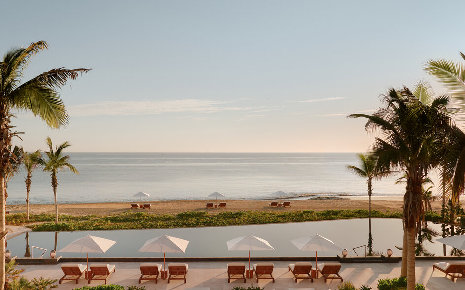 Vista al mar desde Amanvari, resort en México, con palmeras y tumbonas al atardecer.