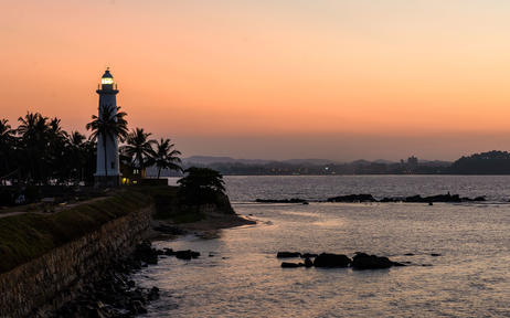 Amangalla's waterfront temple silhouetted against a golden sunset over calm waters.