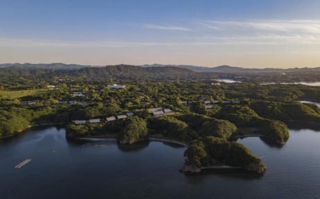 Aerial view of Aman Tokyo's surrounding landscape with forested hills and a tranquil waterway at dusk.