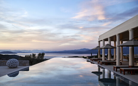 Amanzoe villa with waterfront terrace overlooking calm waters at dusk.