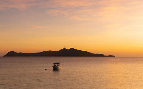 Manamoc Island at sunset, with a small boat on calm waters at Amanpulo.