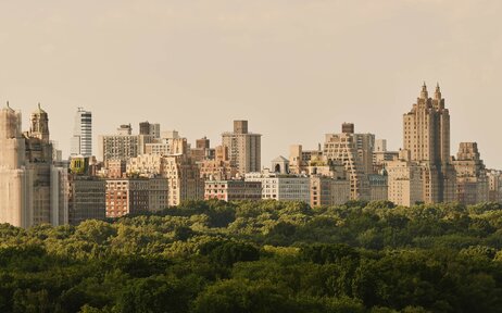 Aman New York residences with Manhattan skyline rising above Central Park greenery.