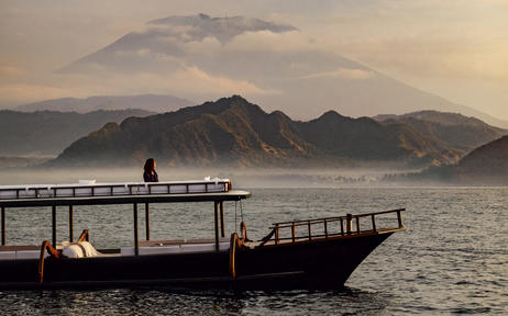Sunrise cruise departure from wooden jetty at Amankila, with misty mountains across calm waters.