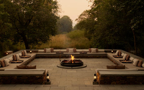 Symmetrical dining pavilion at Aman-i-Khas with central fire pit, stone seating, and tree-lined avenue at dusk.