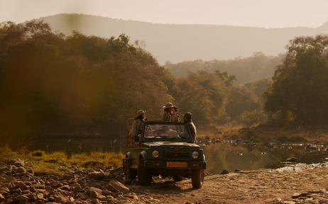 Safari vehicle navigating dusty terrain through forested landscape at Aman-i-Khas, India.