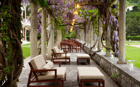 Restaurant terrace at Aman Sveti Stefan with stone columns, flowering vines, and lounge seating overlooking gardens, Montenegro.