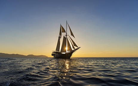 Traditional sailing vessel at Amandira, East Indonesian Archipelago, silhouetted against golden sunset waters.