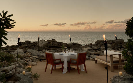 Two red chairs positioned on a sandy beach at sunset, overlooking the ocean at Amanyara resort in Turks and Caicos.
