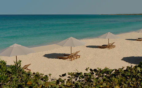 Turquoise waters and pale sand at Amanyara's private beach, with traditional wooden boats anchored offshore.